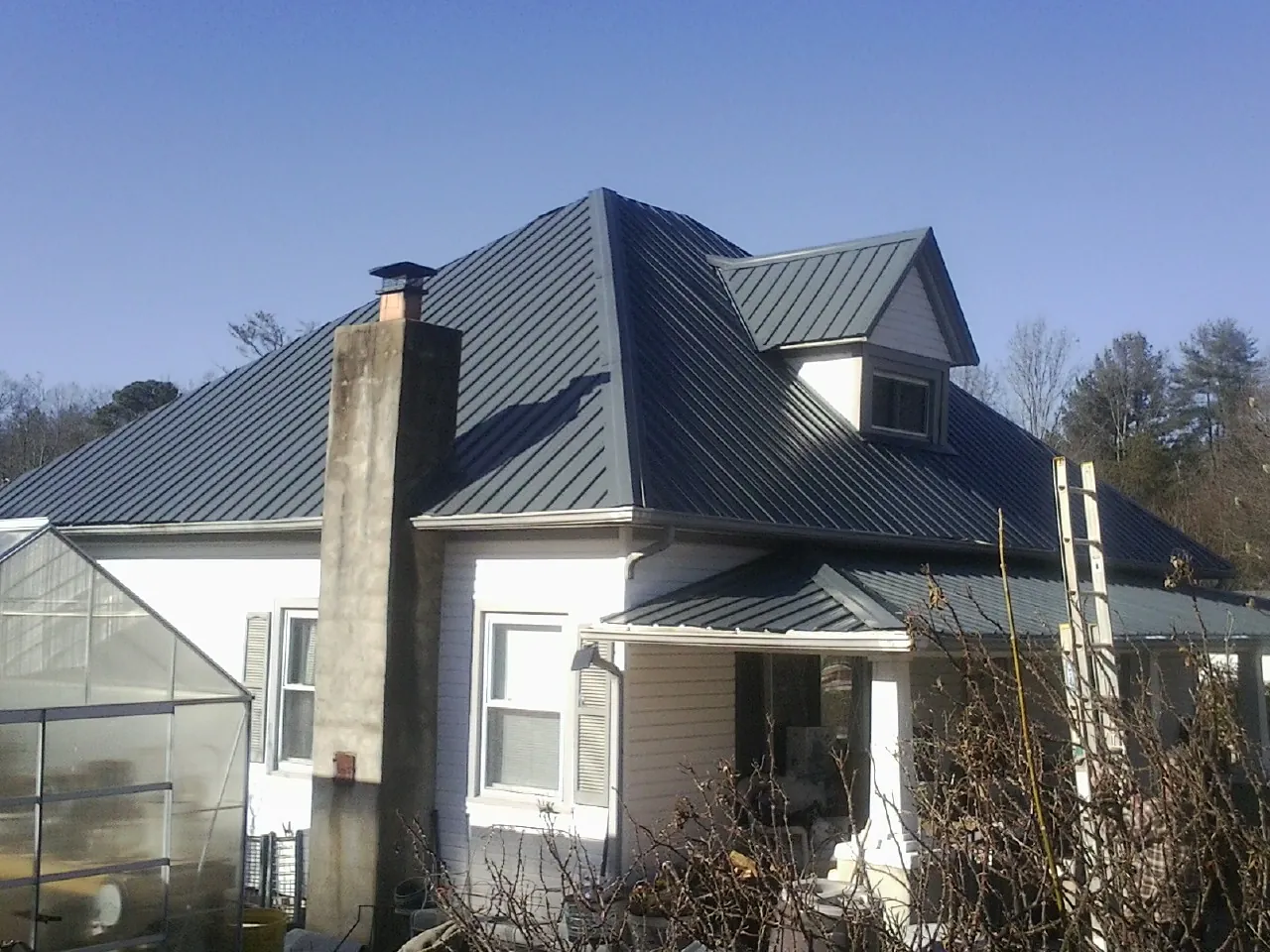 Dark blue standing seam metal roof on a white farmhouse with dormer — Slate & Tile Roof Repair by Roofing Brothers in Stokes