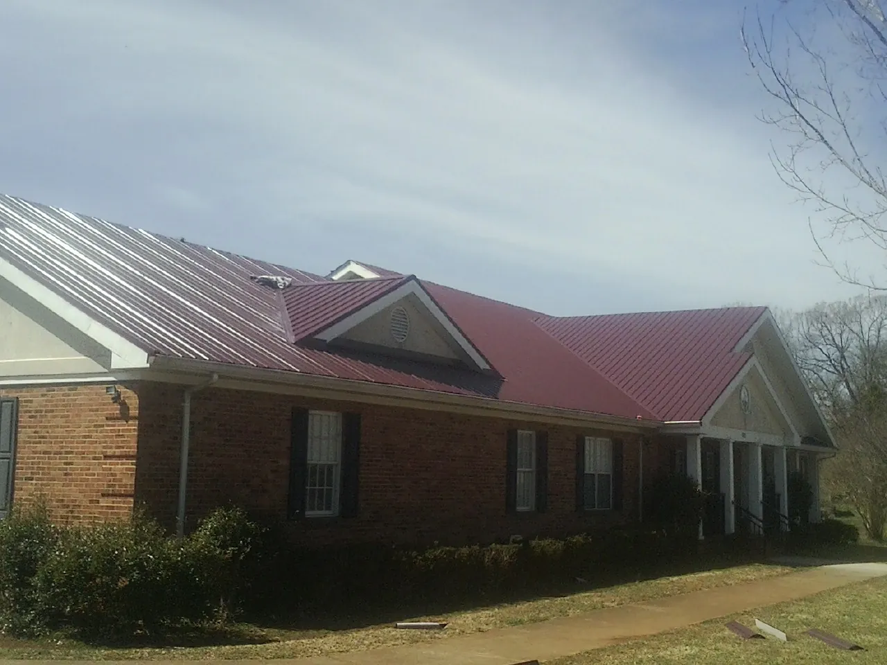 Red metal roof with gabled entries on a long brick building, from a Hail Damage Roof Repair job in Stokes