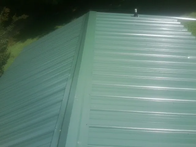 New green metal panels meeting at the ridge of a roof — Flat Roof Repair work by our crew in Stokes