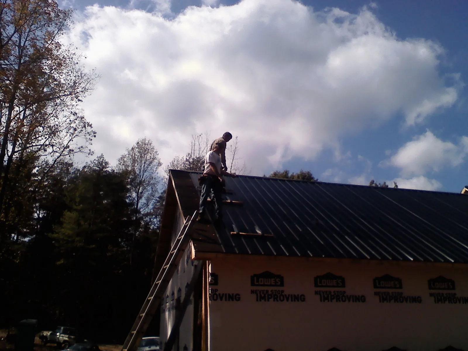 Roofer fastening dark metal panels high against a cloudy sky, from a Roof Inspection job in Stokes